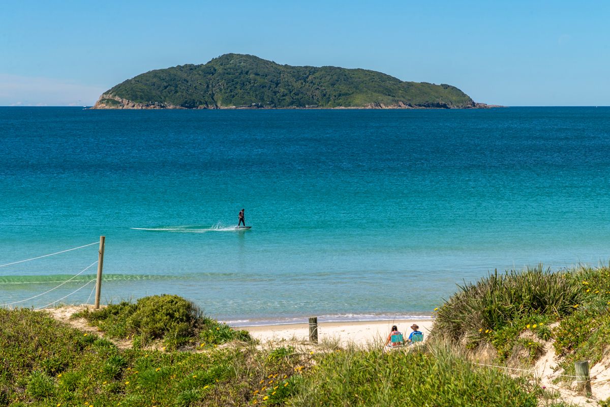 Paddler on clear turquoise water off Bennetts Beach with a wooded island beyond